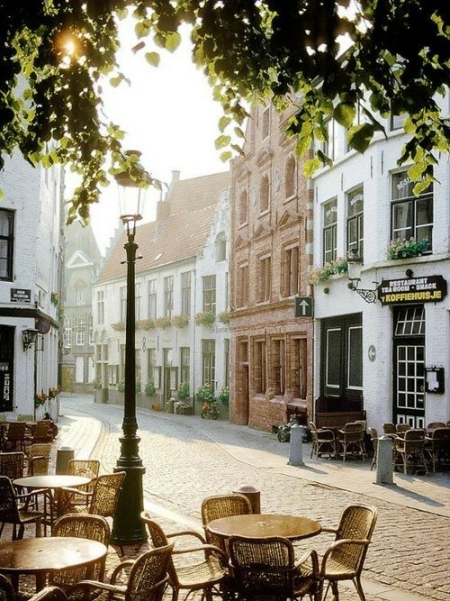 A serene street scene showcasing charming man-made architecture bathed in morning light, framed by vibrant greenery and outdoor café tables.