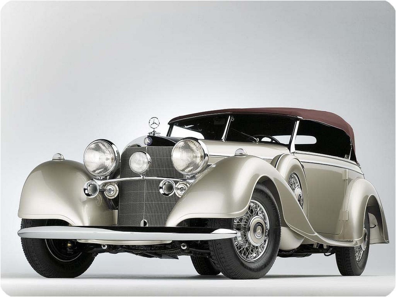 A classic Mercedes-Benz 500K convertible with polished chrome details and a maroon soft top against a plain light background.