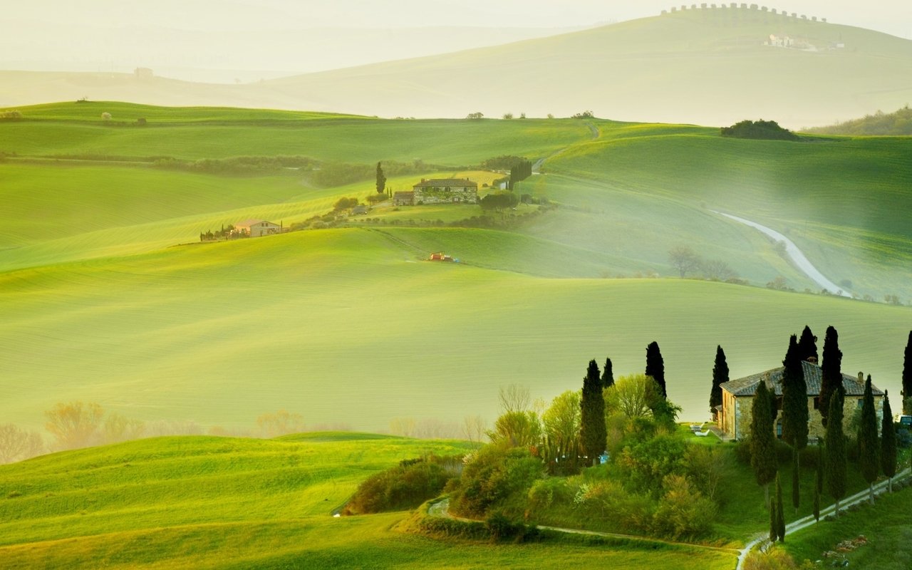 A serene Tuscan landscape featuring rolling green hills, cypress trees, and a misty atmosphere that captures the enchanting beauty of the region's rural charm.