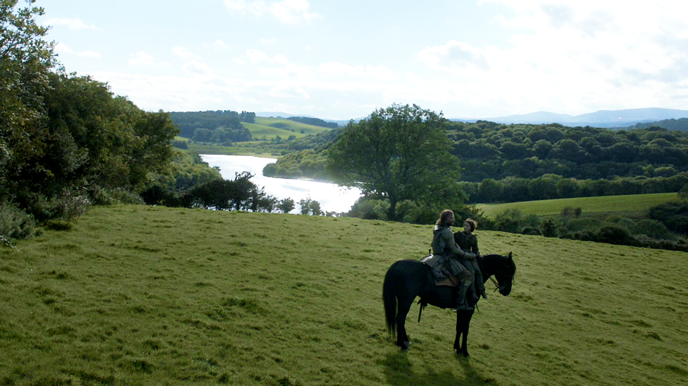 Rory McCann as Sandor Clegane and Maisie Williams as Arya Stark ride on a horse, overlooking a scenic landscape in a scene from the TV show Game of Thrones.