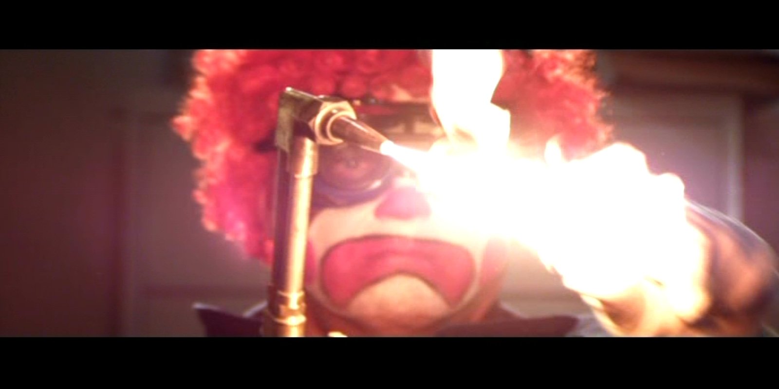 A scene from the movie Parker featuring a clown with a red wig and exaggerated makeup, illuminated by bright flames near a torch.