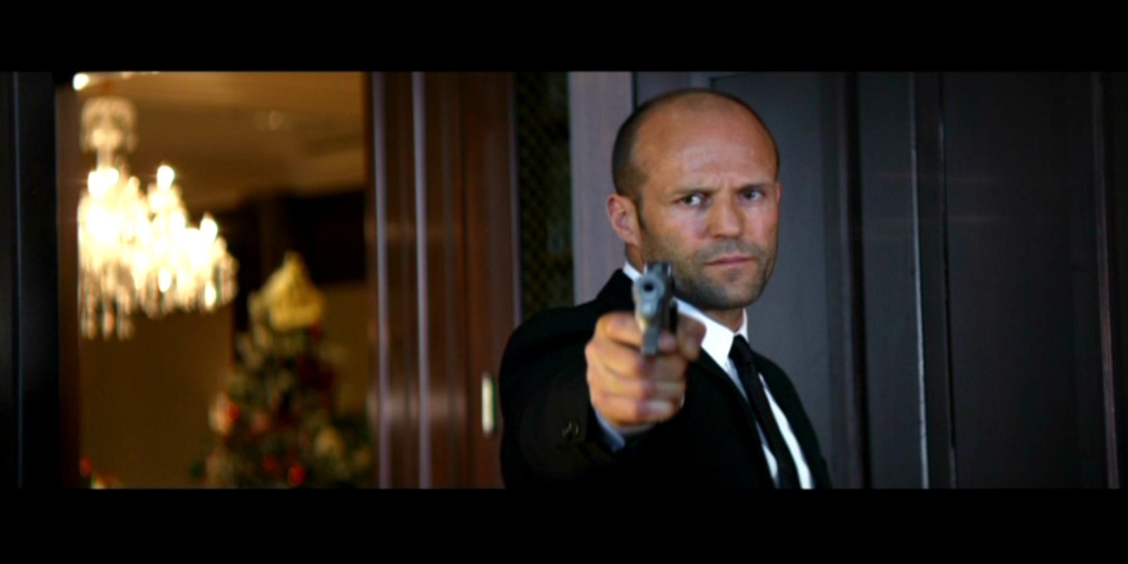 Scene from the movie Parker showing a determined man in a suit aiming a gun inside a dimly lit room.