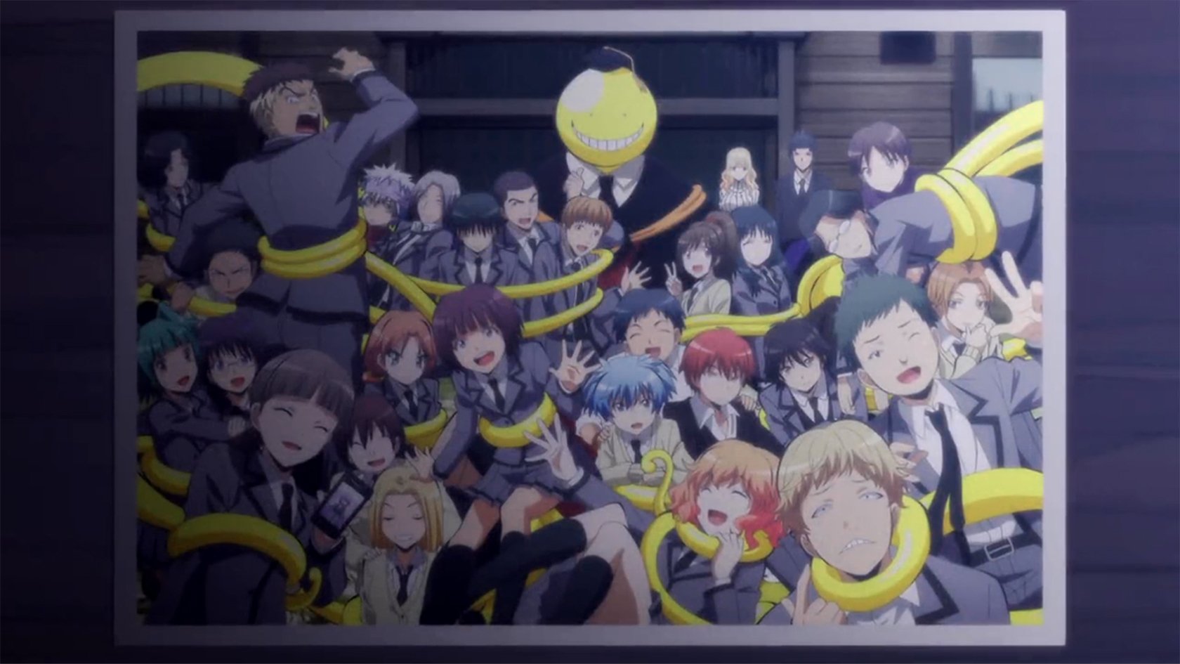 Anime group photo of Class 3-E from Assassination Classroom, students crowded around their smiling yellow teacher Koro-sensei in a lively classroom portrait.