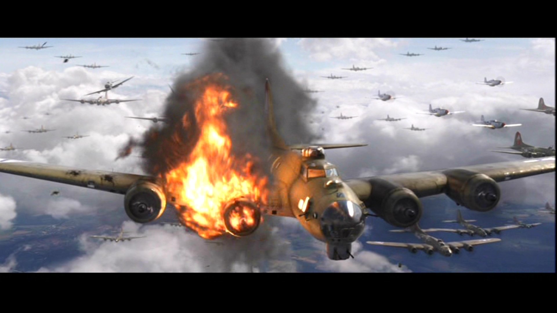 Still from the movie Red Tails: a World War II bomber trailing smoke and flames amid a formation of fighter planes over cloud cover.