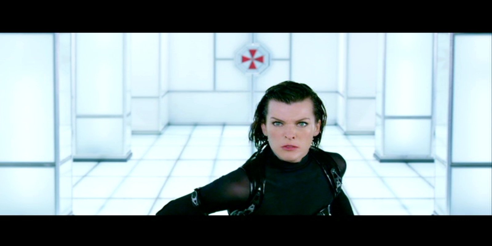 Scene from the movie Resident Evil: Retribution featuring a determined woman in tactical gear standing in a futuristic white room with the Umbrella Corporation logo on the wall.