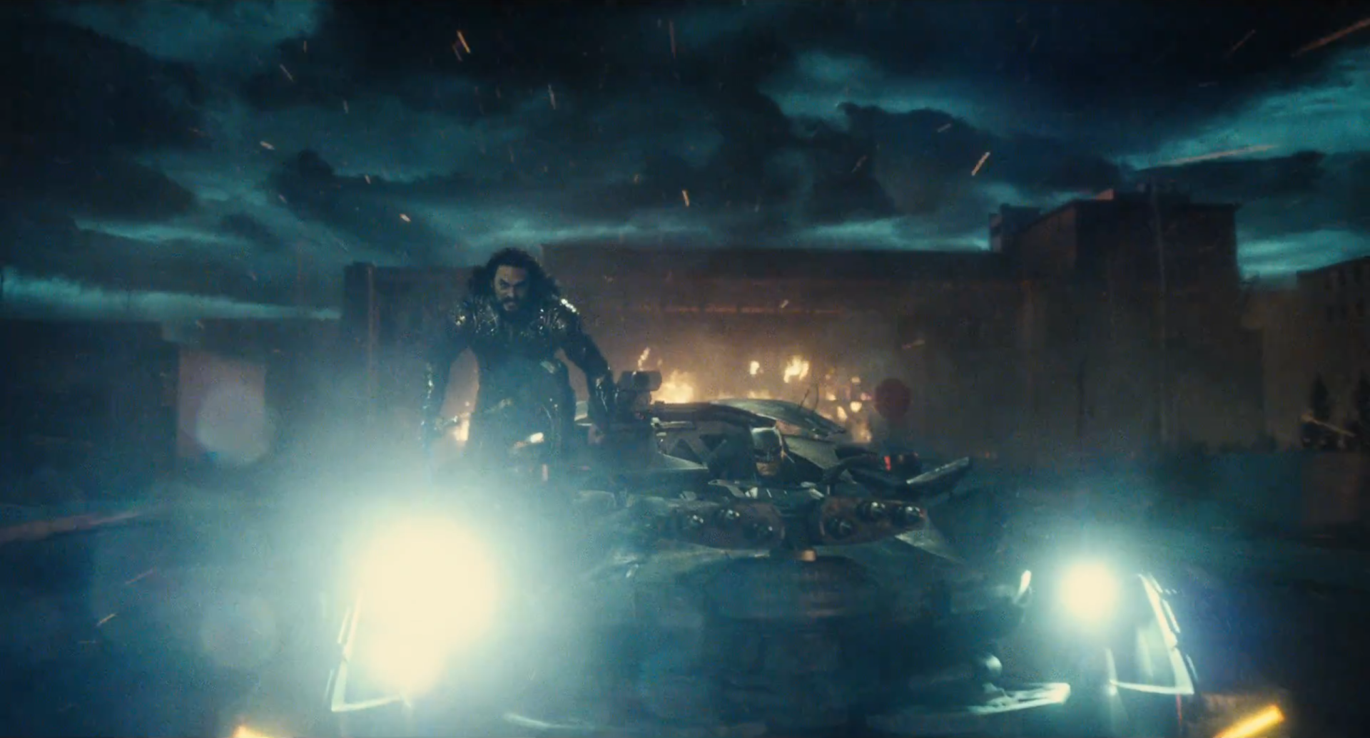Jason Momoa’s Aquaman stands beside the Batmobile driven by Ben Affleck’s Bruce Wayne in the dark, atmospheric scene from the 2017 DC Comics Justice League movie.