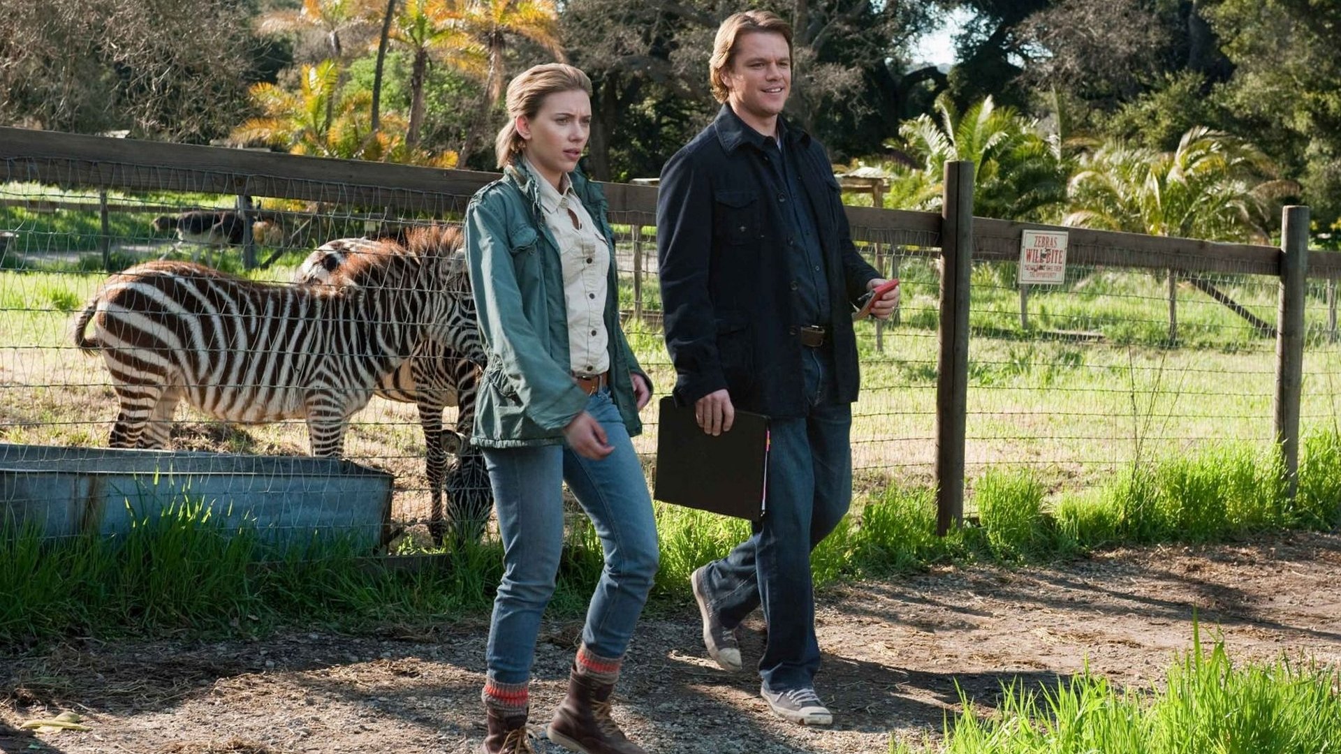 Matt Damon and Scarlett Johansson walk together near a zebra enclosure in a scene from the movie We Bought A Zoo.