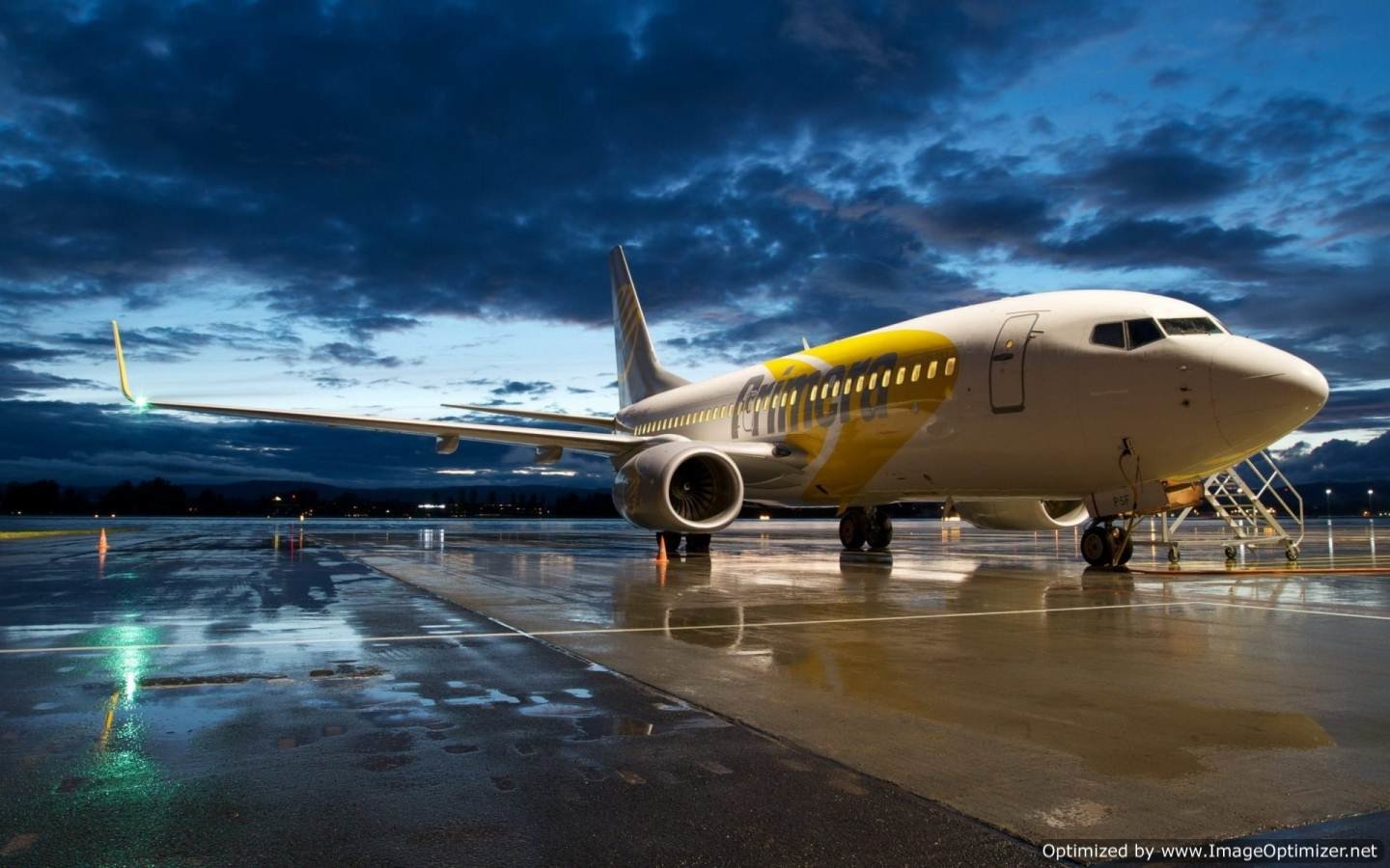 A parked airplane rests on a wet runway under a dramatic cloudy sky during twilight.