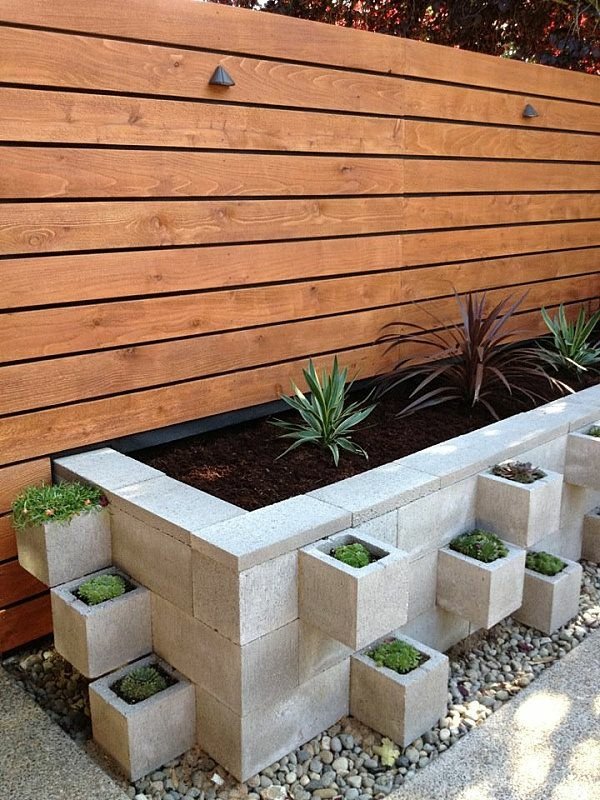 Modern landscaped garden with a man-made concrete planter box of succulents and stacked cinderblock planters against a horizontal wooden fence.