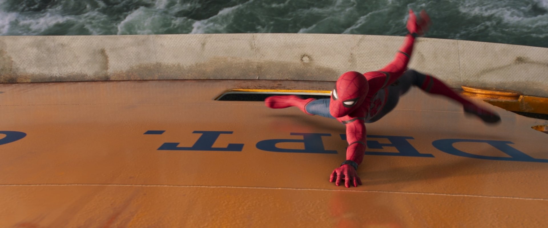 Spider-Man in action clinging to the side of a moving school bus, a scene from the movie Spider-Man: Homecoming.