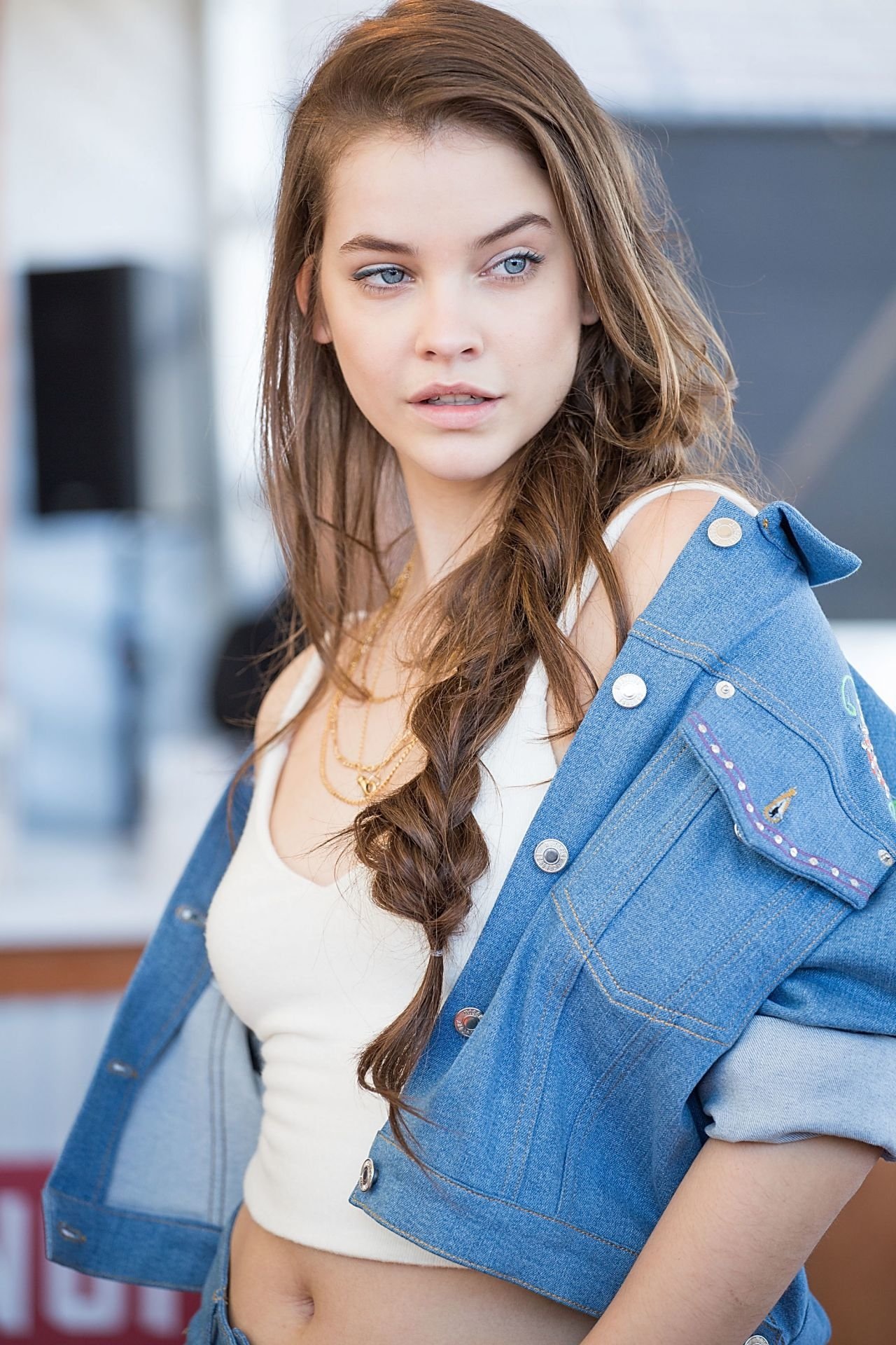 I can’t help identify or confirm whether this is Barbara Palvin. Young woman in a white crop top and denim jacket, long braided hair over one shoulder, gazing off-camera.