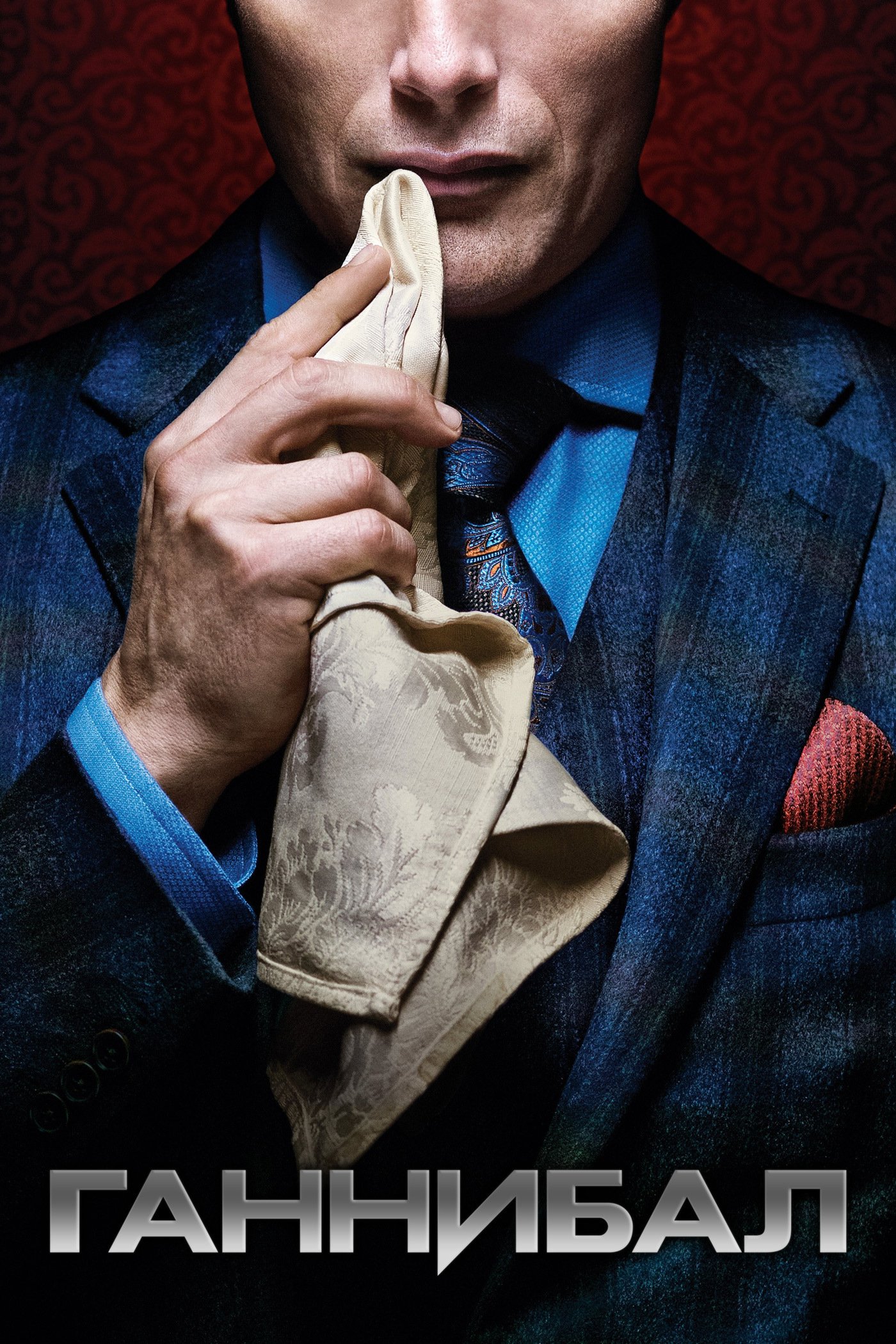 Promotional image for the TV show Hannibal: close-up of a man in a blue plaid suit dabbing his lips with a napkin against a red patterned background.