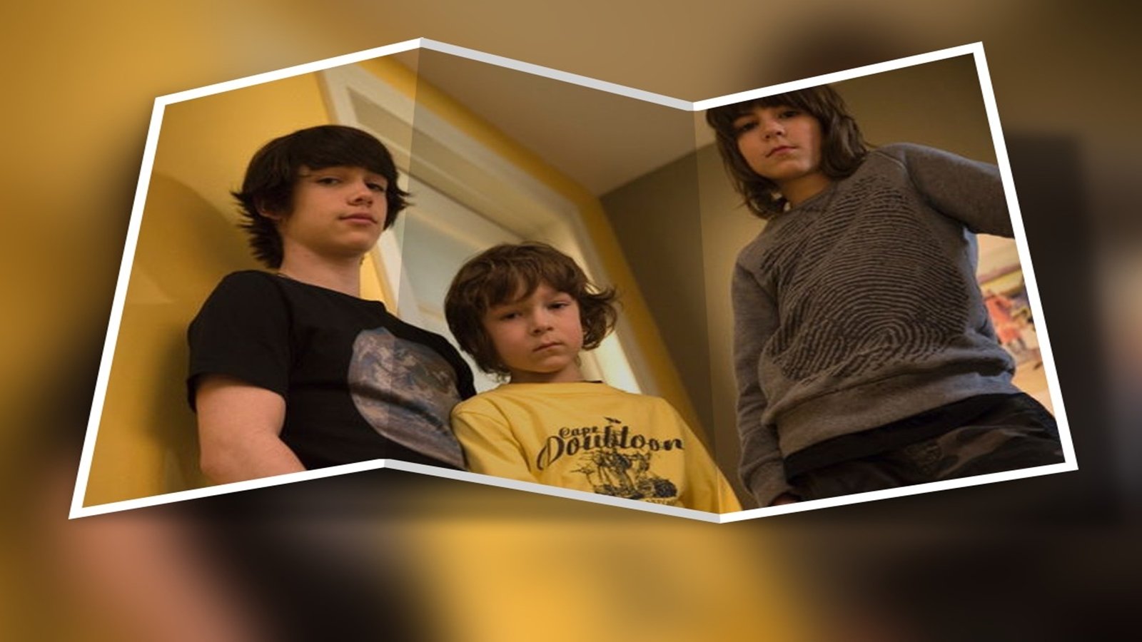 Three boys from the TV show Les Parent stare down at the camera in a tilted photo-style frame, inside a yellow-walled room.