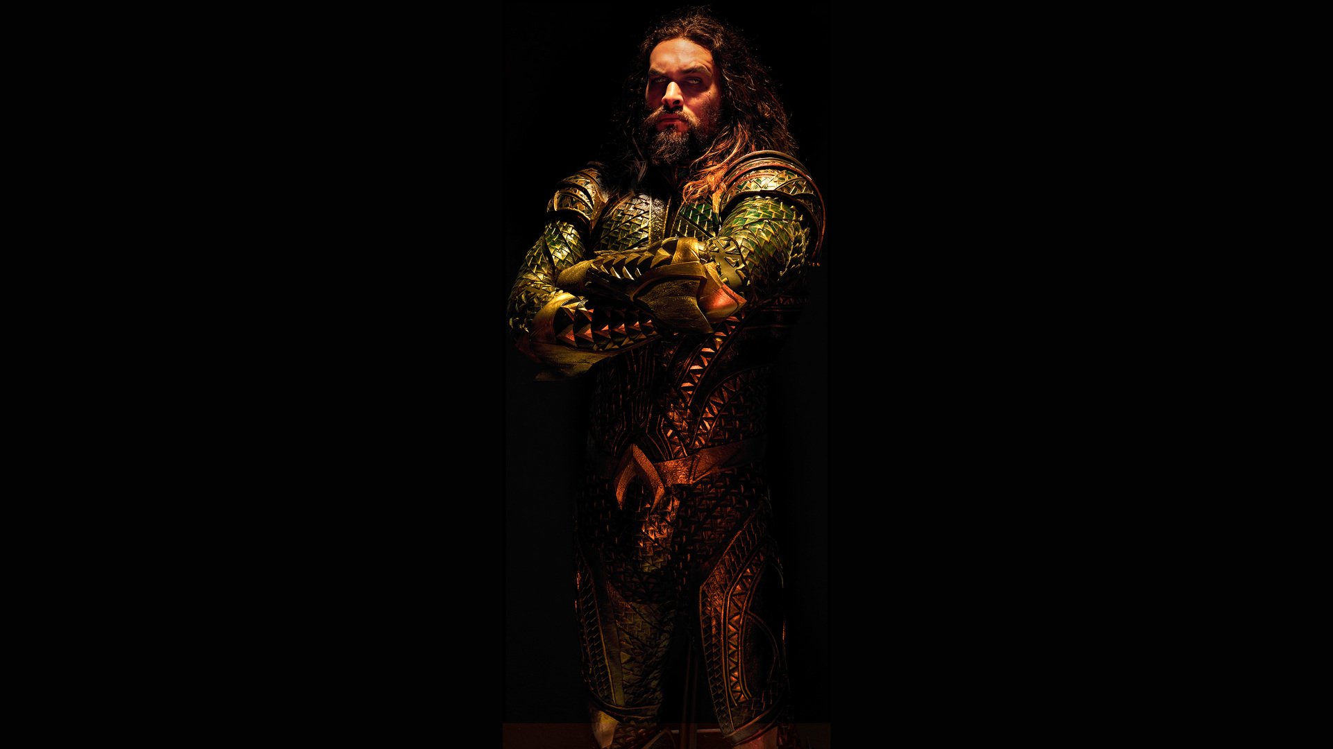 Jason Momoa as Aquaman in a dark setting from the 2017 Justice League movie, showcasing his armored costume with crossed arms.