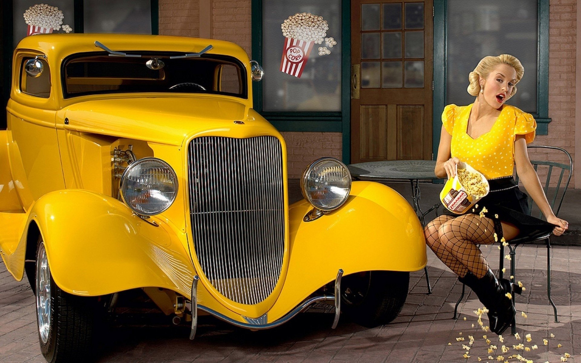A woman in a yellow top and fishnet tights sits near a classic yellow car, spilling popcorn in a vintage-style setting with popcorn-themed wall art.