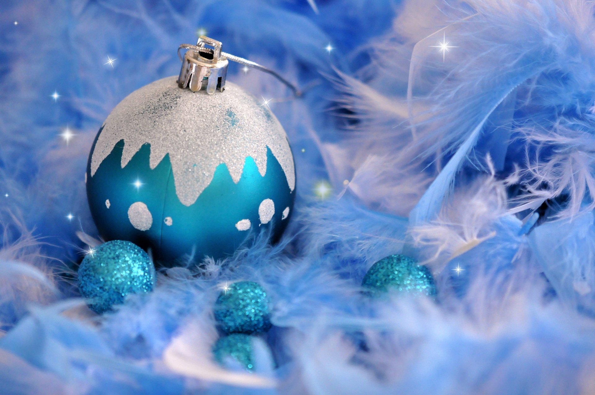 A white and blue Christmas ornament surrounded by blue feathers and small glittery blue holiday decorations.