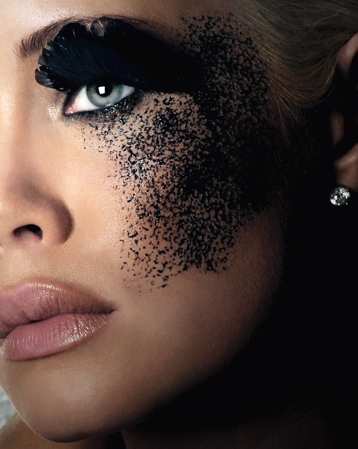 A close-up of model Katharine Lowrey showcasing bold makeup, featuring striking black eyelashes and artistic shadow detailing on her cheek.