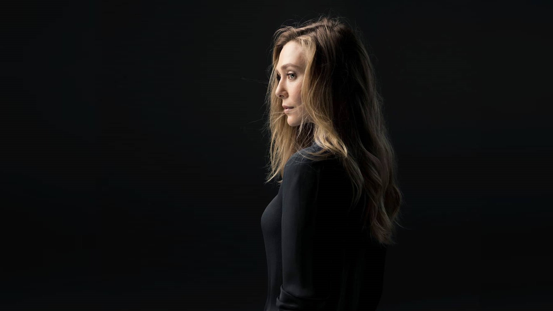 Elizabeth Olsen is shown in profile against a dark background, with soft lighting highlighting her face and hair.