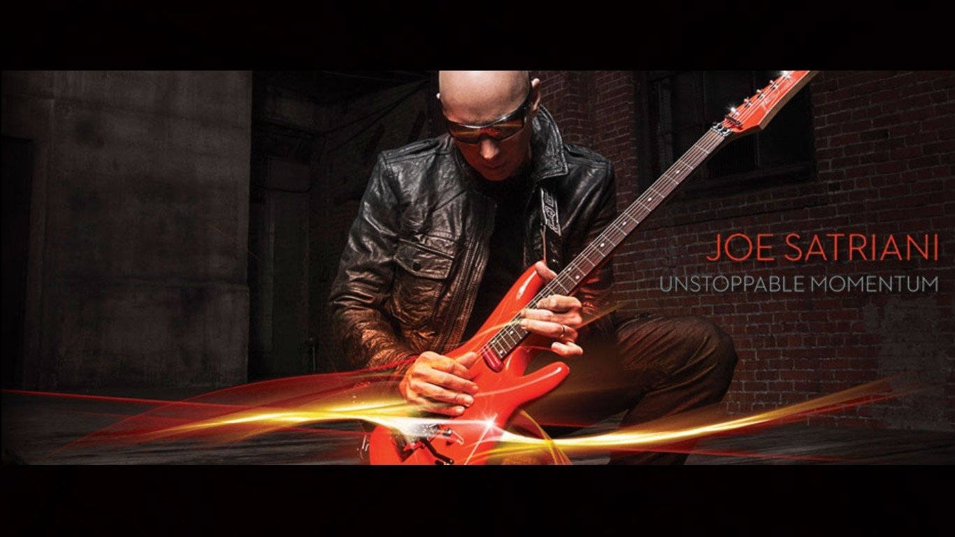 A dynamic image of Joe Satriani passionately playing an orange guitar, embodying the energy of music with the text Unstoppable Momentum alongside him.
