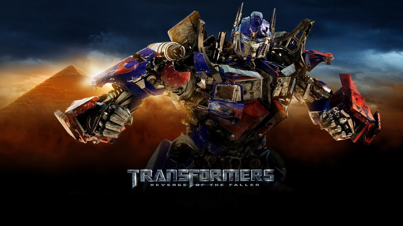 Poster for the movie Transformers: Revenge of the Fallen — Optimus Prime in blue-and-red armor stands with weapons before pyramids under a stormy sky.