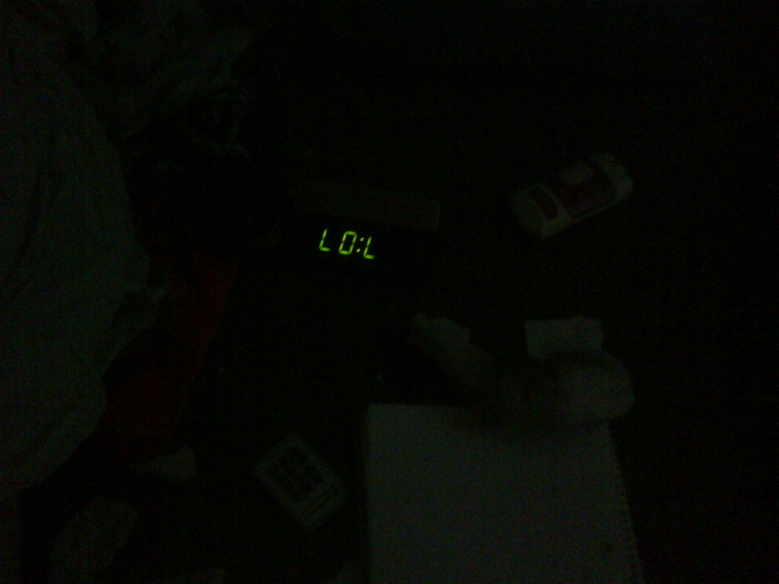 A humorous scene with a digital clock displaying L:0:L in dim light, surrounded by scattered items, giving a playful vibe to the cluttered space.