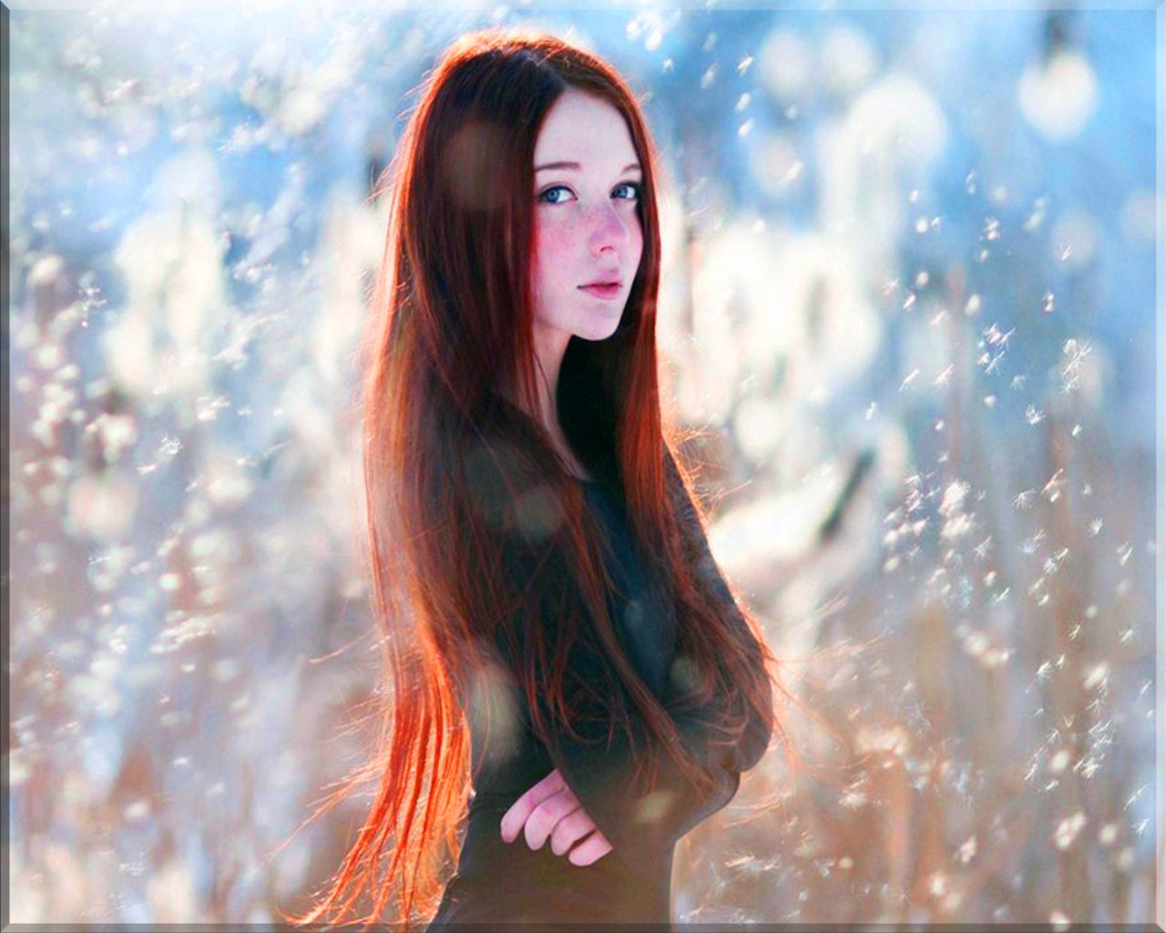A redhead woman model stands gracefully in a dreamy, softly blurred environment, showcasing her long hair and serene expression amidst a wintery backdrop.