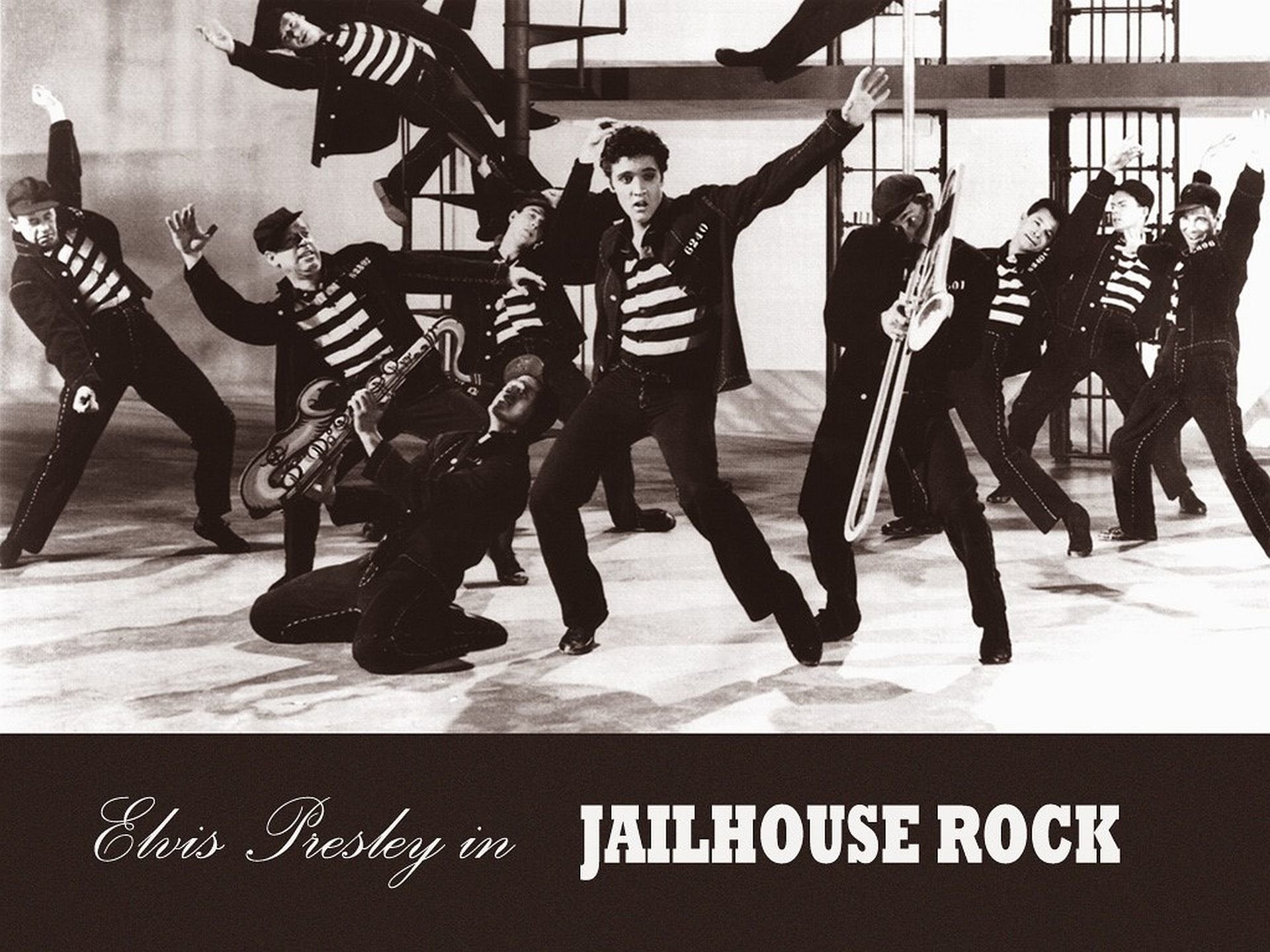 Black and white image of Elvis Presley and dancers in striped jail uniforms performing a scene from the Rock & Roll movie Jailhouse Rock.