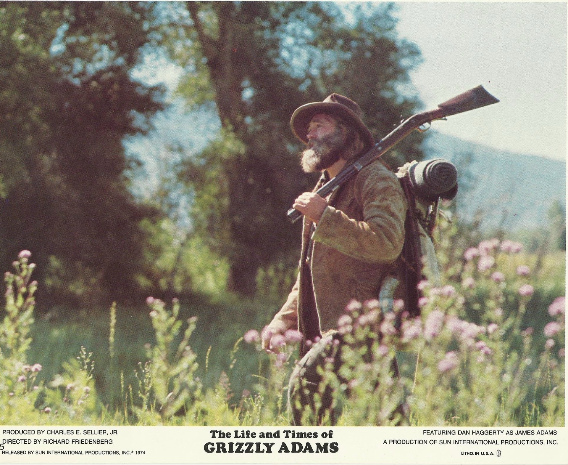 Bearded frontiersman with rifle and pack walks through a wildflower meadow — promotional image for the TV show The Life and Times of Grizzly Adams.