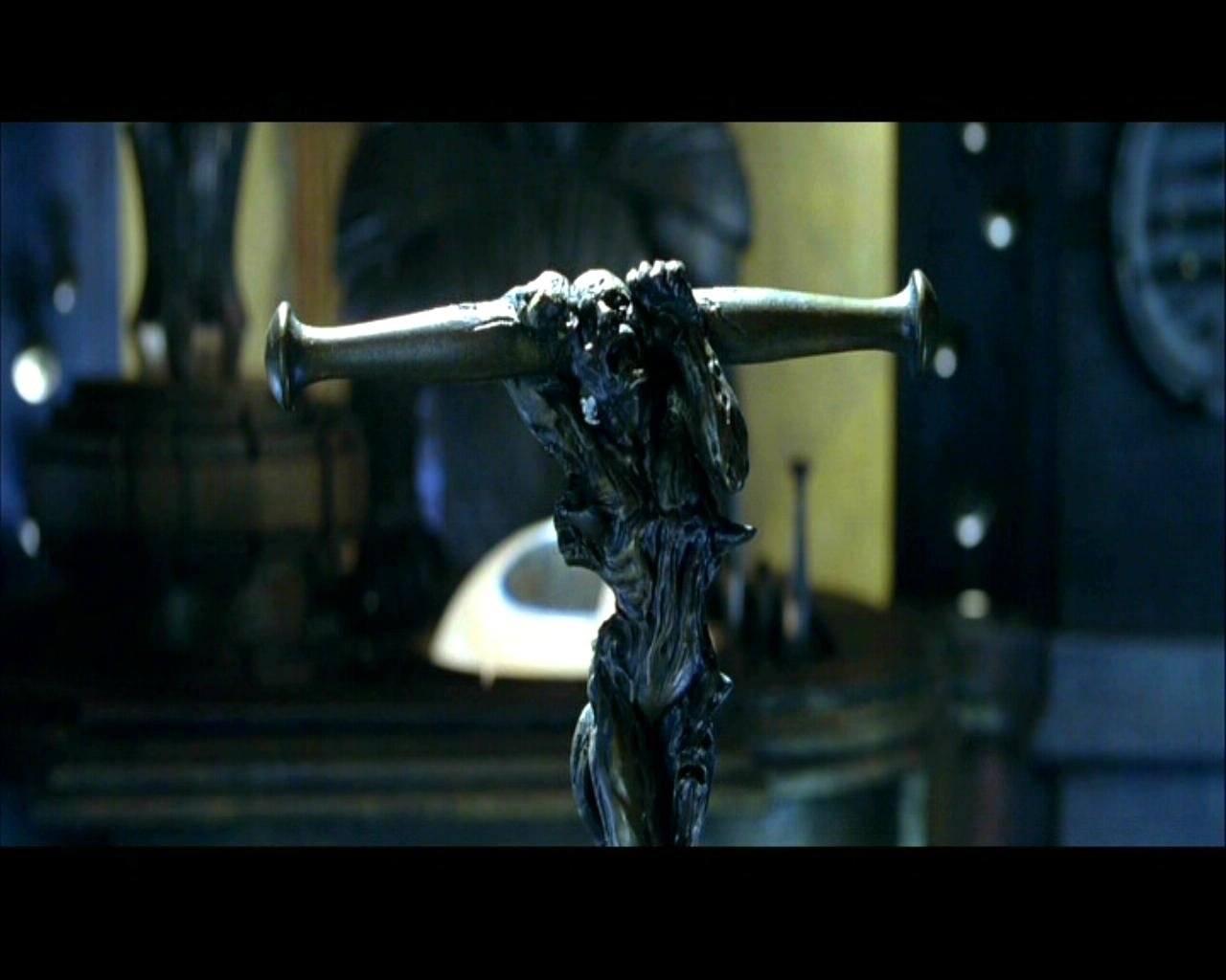 Close-up of a dark, twisted metallic sculpture mounted on a pole in a dim, industrial interior — a scene from the movie The Chronicles Of Riddick.