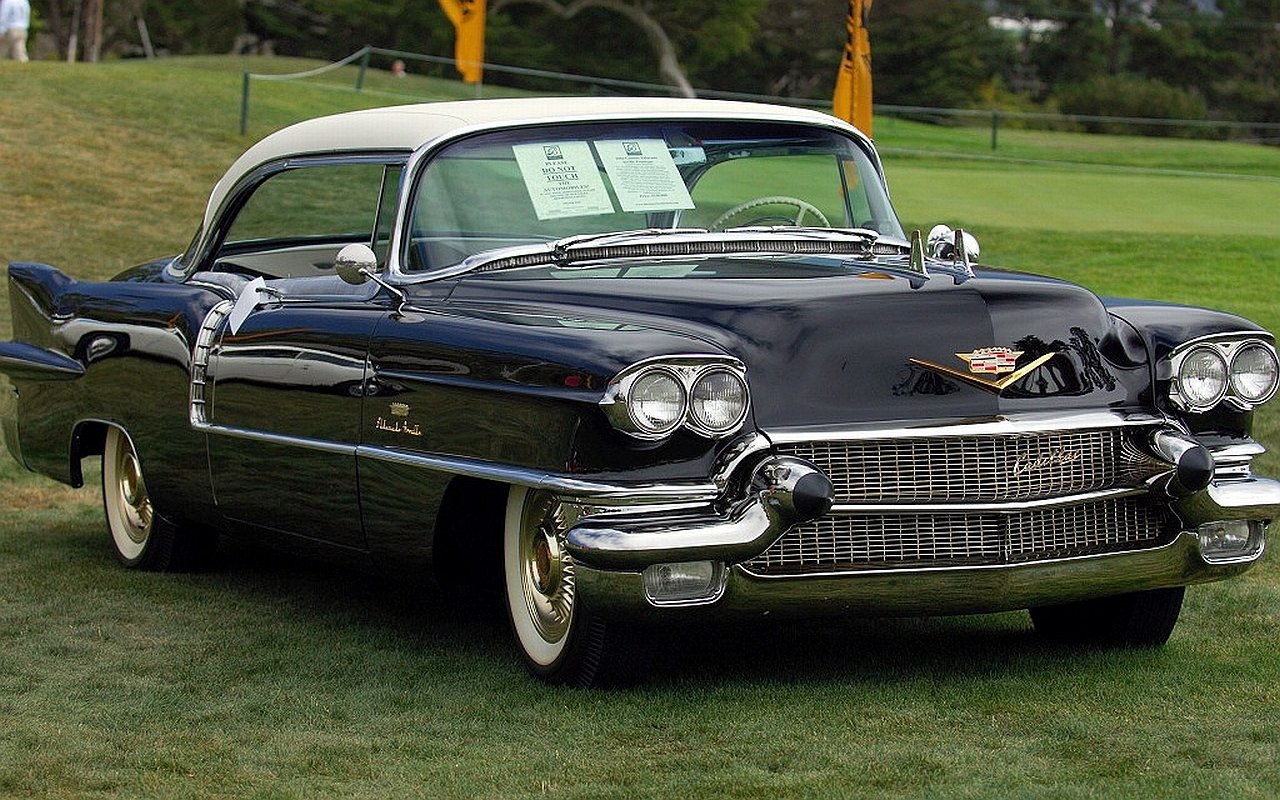 Shiny dark-blue classic Cadillac vehicle with white roof, prominent chrome grille and whitewall tires parked on grass at a car show.