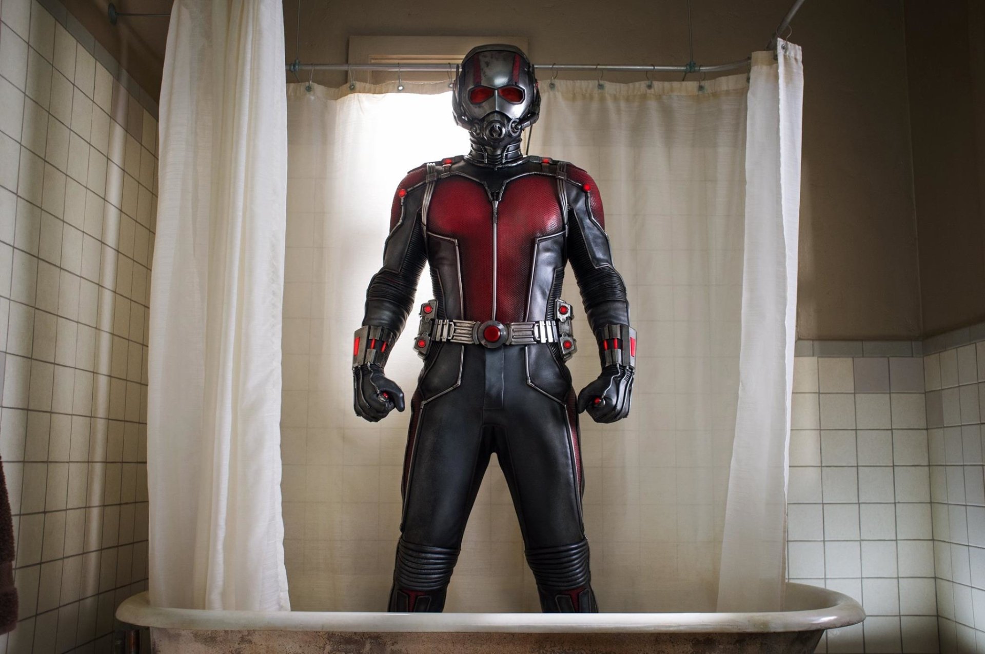 Ant-Man stands confidently in his red and black suit inside a vintage bathroom with light streaming through a window behind him.