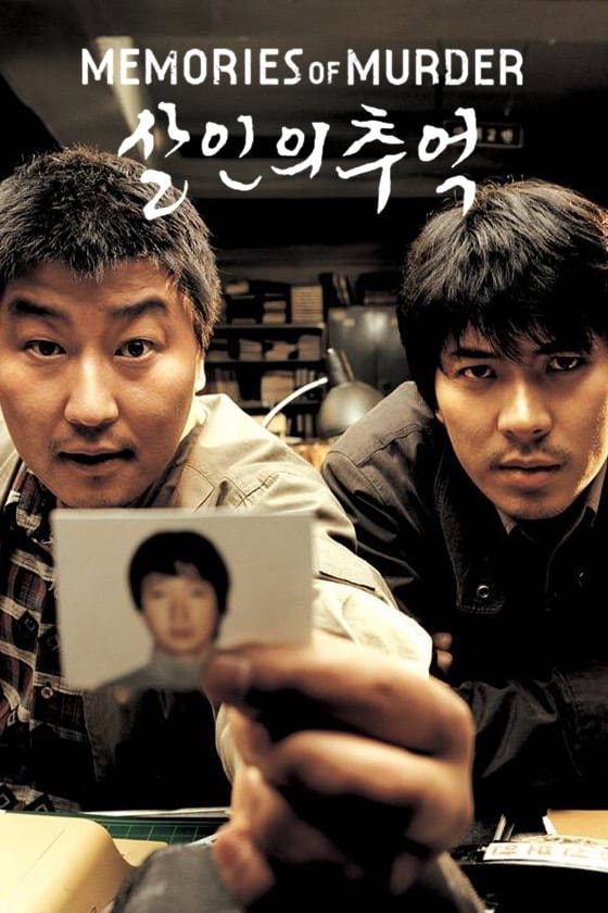 Poster for the movie Memories of Murder: two intense men lean toward the camera as one holds a blurred photo in a dim, cluttered office, evoking a tense investigative mood.