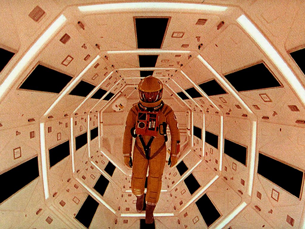 An astronaut walks through a futuristic corridor, reminiscent of the iconic scenes from the movie 2001: A Space Odyssey, featuring geometric patterns and soft lighting.