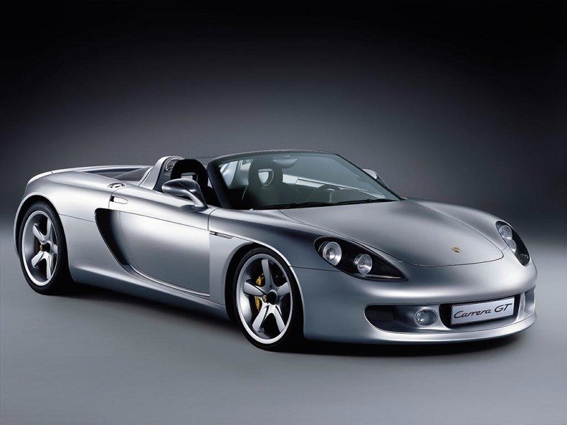 A sleek silver Porsche Carrera GT displayed against a dark background, showcasing its aerodynamic design and convertible features.