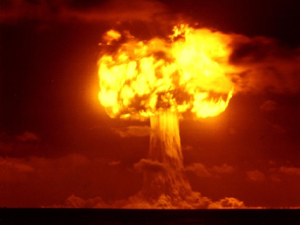 A dramatic mushroom cloud rises from a military explosion, casting an ominous glow against the dark sky, symbolizing the destructive power of nuclear weapons.