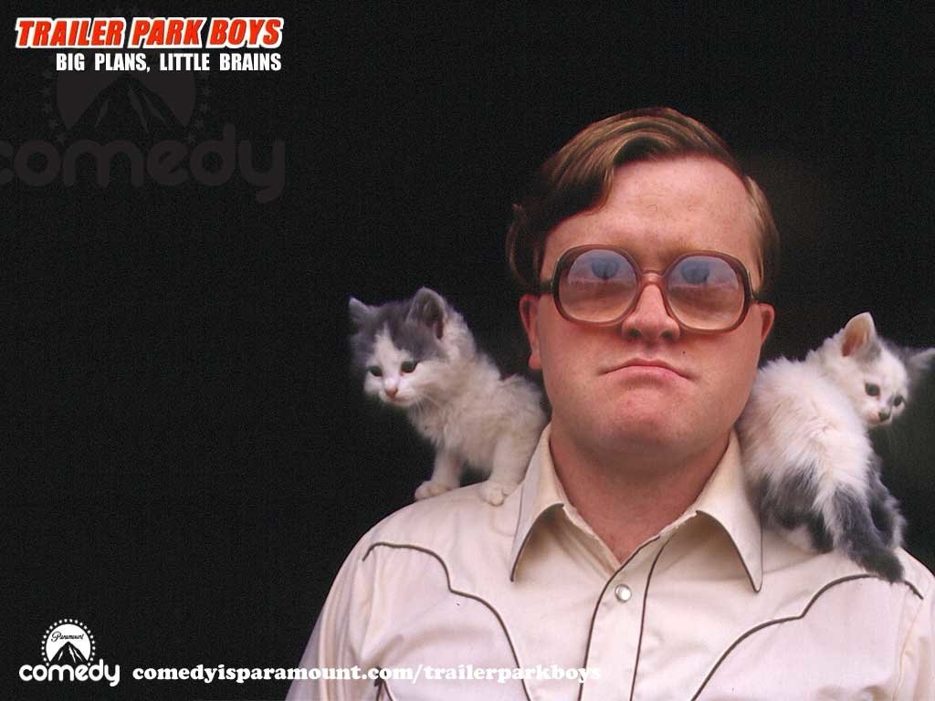 A character from Trailer Park Boys stands confidently, sporting oversized glasses, with two playful kittens perched on his shoulders against a dark background.