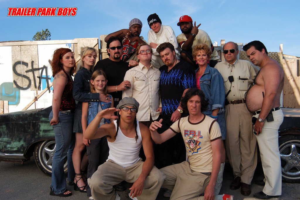 A lively cast of characters from the TV show Trailer Park Boys poses together, showcasing their unique styles and personalities in a fun, outdoor setting.