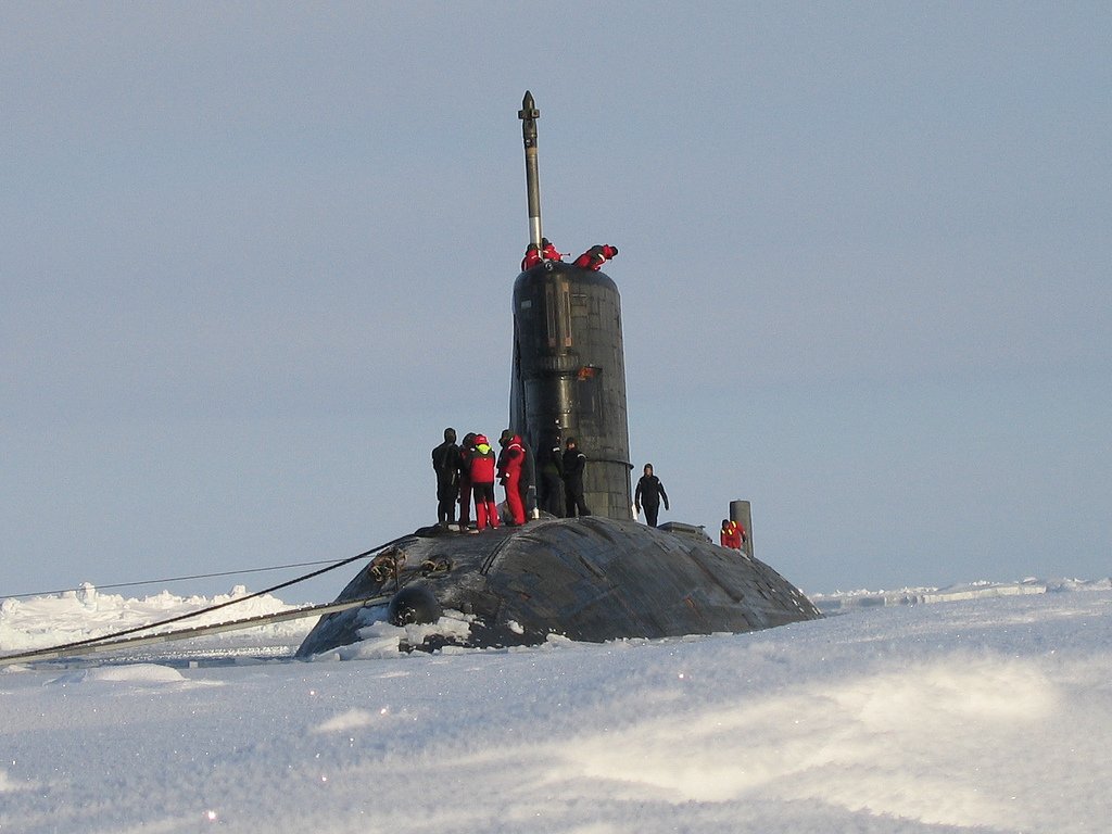 A military submarine surfaces through the snow in the Arctic, with crew members on the deck, showcasing the challenging environment of polar operations.