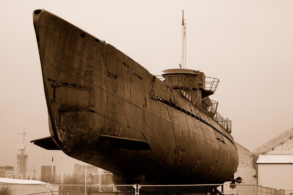 A weathered military submarine rests on land, showcasing its robust structure and historical significance against a muted backdrop.