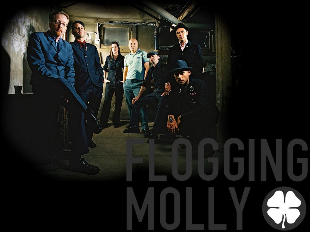 A group of musicians from Flogging Molly poses together in an industrial setting, showcasing their unique blend of punk and Celtic influences.