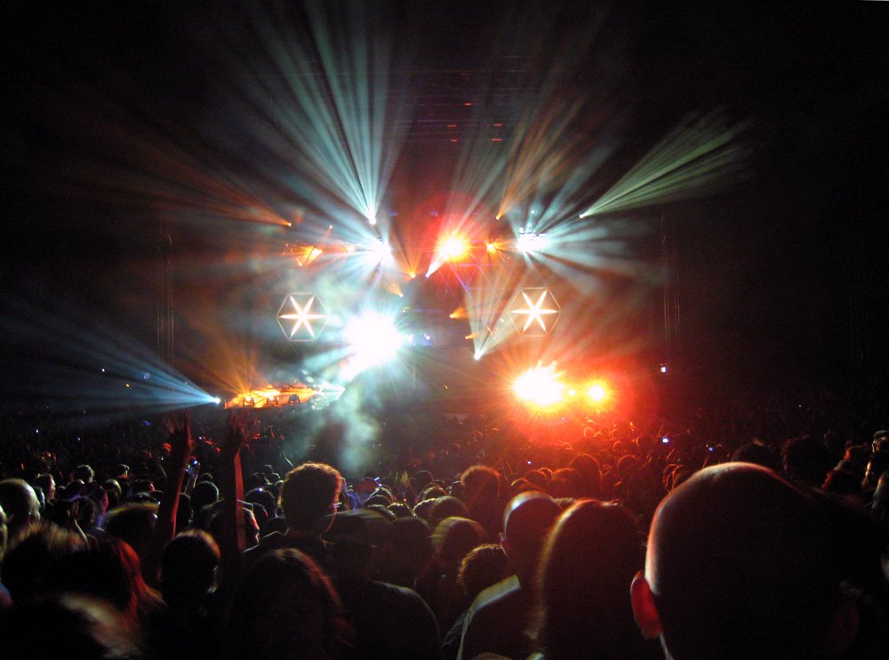 A vibrant concert scene featuring a crowd captivated by dynamic light displays, celebrating the music of Daft Punk. The atmosphere is electric with energy and excitement.