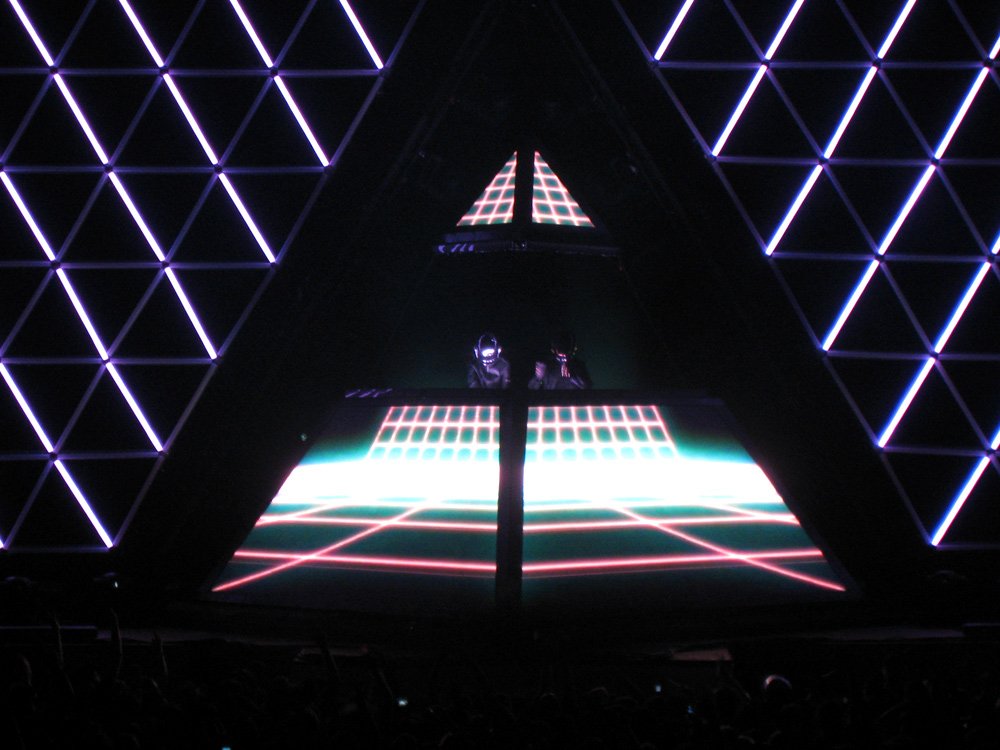 A vibrant stage setup featuring Daft Punk, with a triangular design and colorful lights, highlighting their iconic electronic music performance.