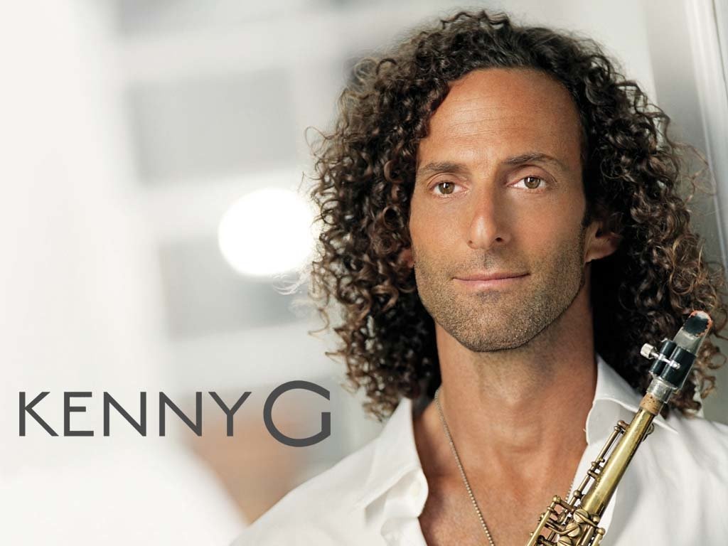 Kenny G, the renowned musician, holds his saxophone and looks confidently at the camera against a softly blurred background.
