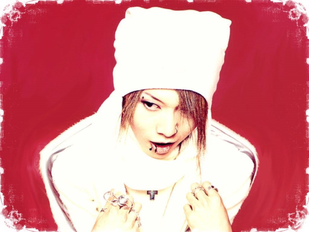 Portrait of Miyavi, the J-Rock musician, wearing a white outfit and hat against a red background.
