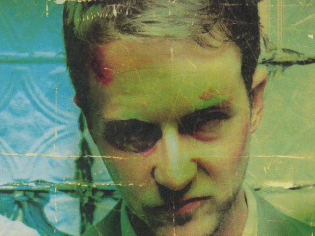 A close-up of a man with a tense expression, showing signs of injury, against a textured blue background. This image relates to the movie Fight Club.
