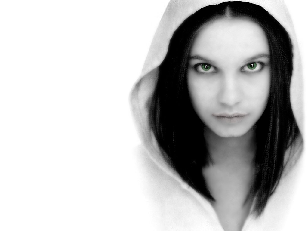 A sensual woman with striking green eyes gazes intensely at the viewer, partially obscured by a white hood that adds an air of mystery to her captivating presence.