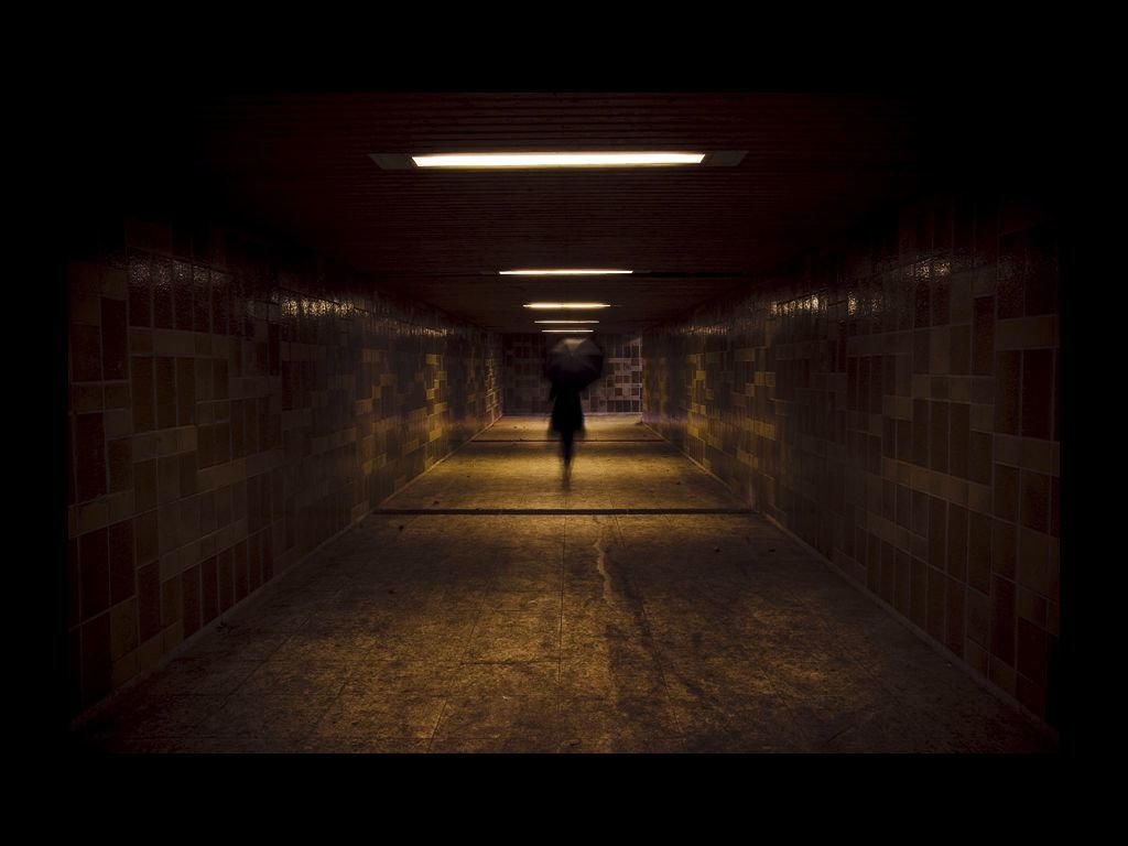 A dimly lit, man-made underground corridor with a shadowy figure walking through, evoking a dark and eerie atmosphere reminiscent of the Dark Scares Hotel.