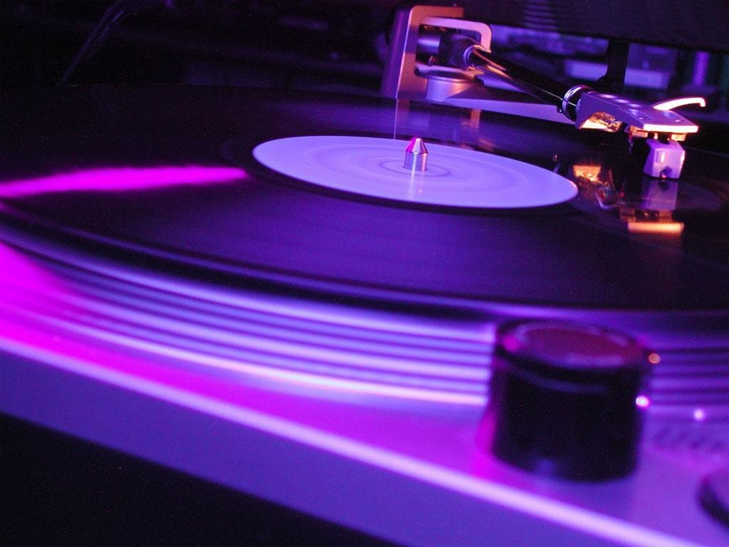 Close-up of turntables with a spinning vinyl record, illuminated by dynamic purple lighting, capturing the energy of a DJ and the vibrancy of music.