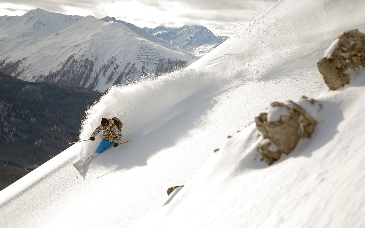 A skier carves through fresh powder on a snow-covered slope, surrounded by majestic mountains, showcasing the thrill of winter sports.