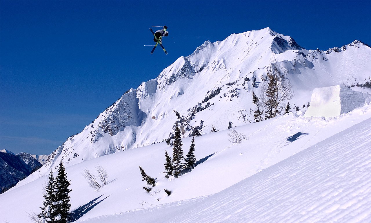 A skier performs an aerial jump against a stunning snowy mountain backdrop, showcasing the thrill of winter sports and skiing in an alpine landscape.